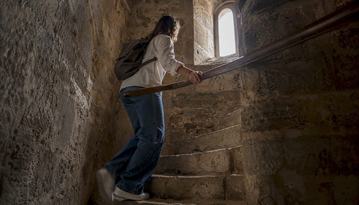 Visitor climbing narrow stone castle stairs
