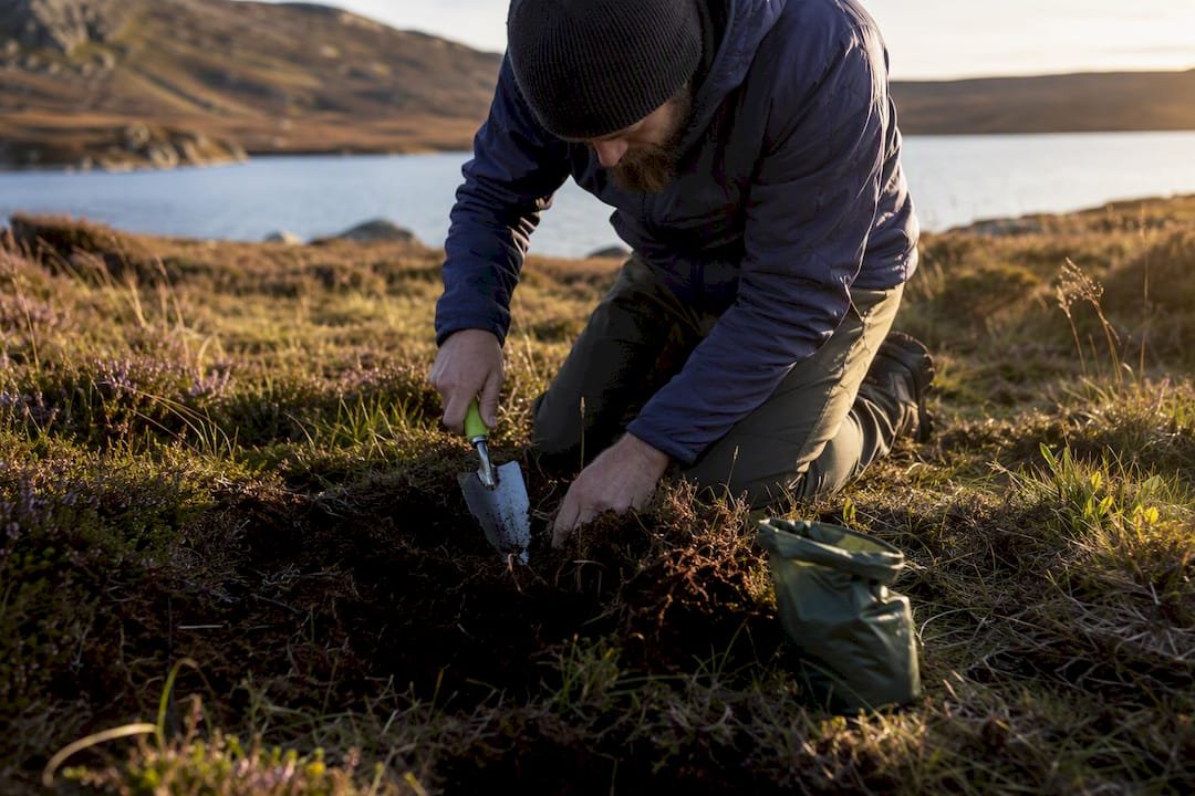 Camper digging cathole near stream